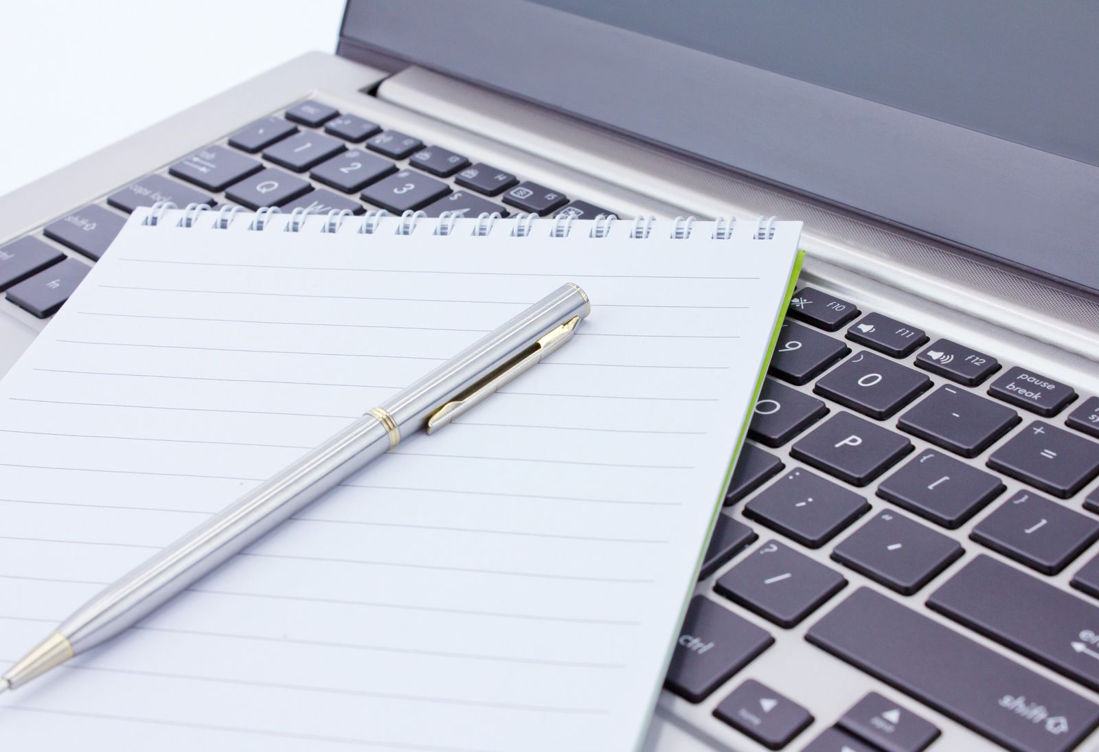 pen resting on a blank note bad resting on top of an open laptops keyboard