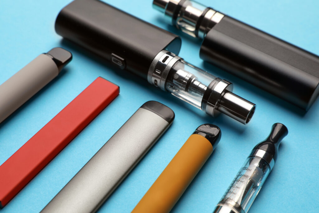 Different electronic cigarettes on light blue background, closeu