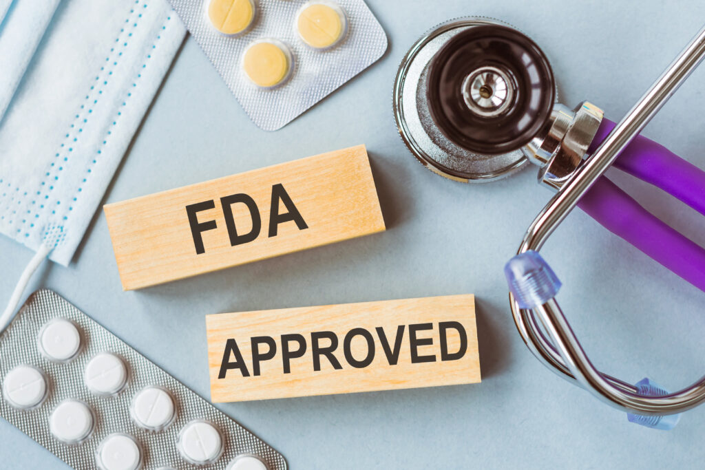 FDA Approved phrase is written on two wooden blocks that lie on a light blue background together with pills, stethoscope and medical mask