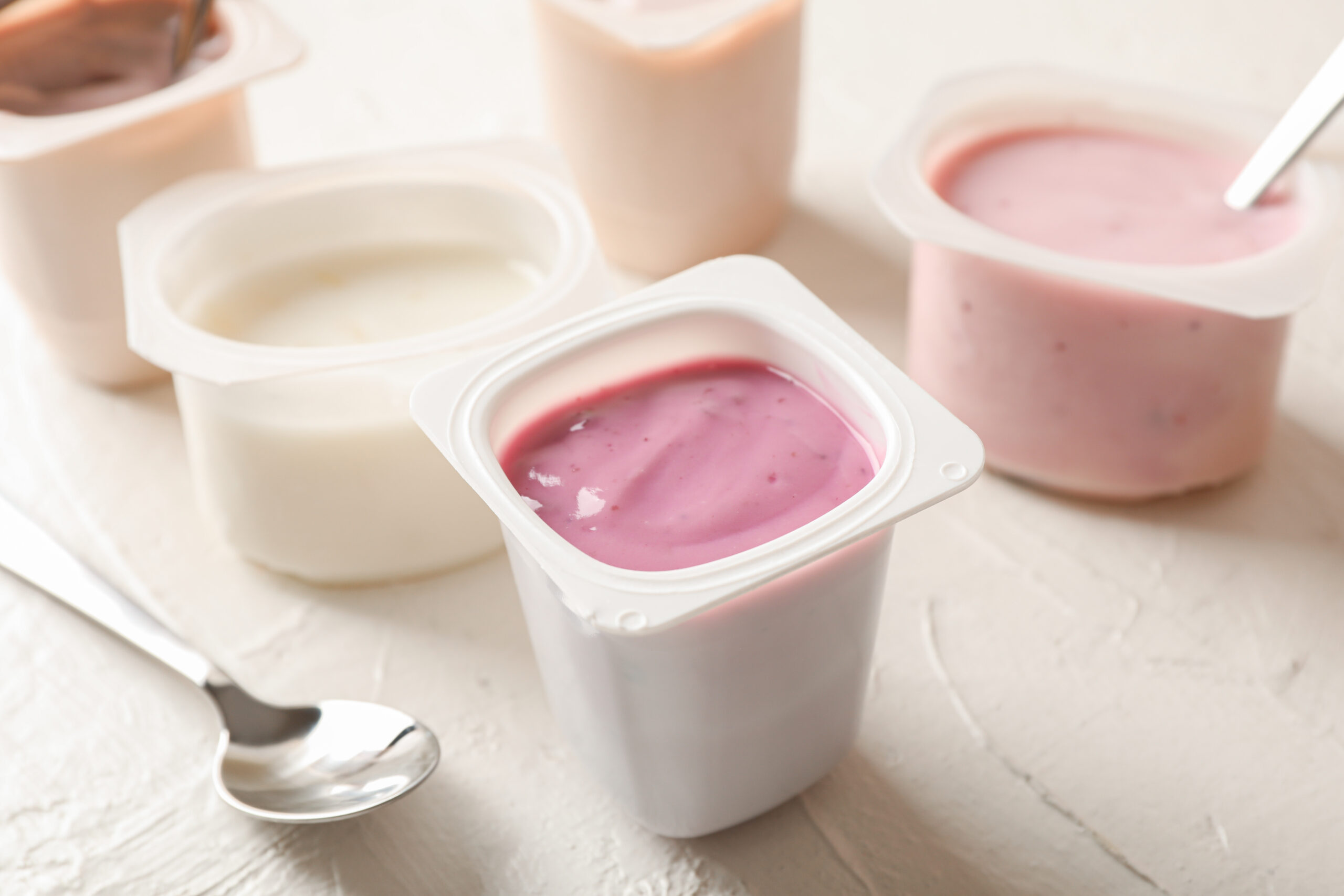 Composition with plastic cups with yogurt on white table