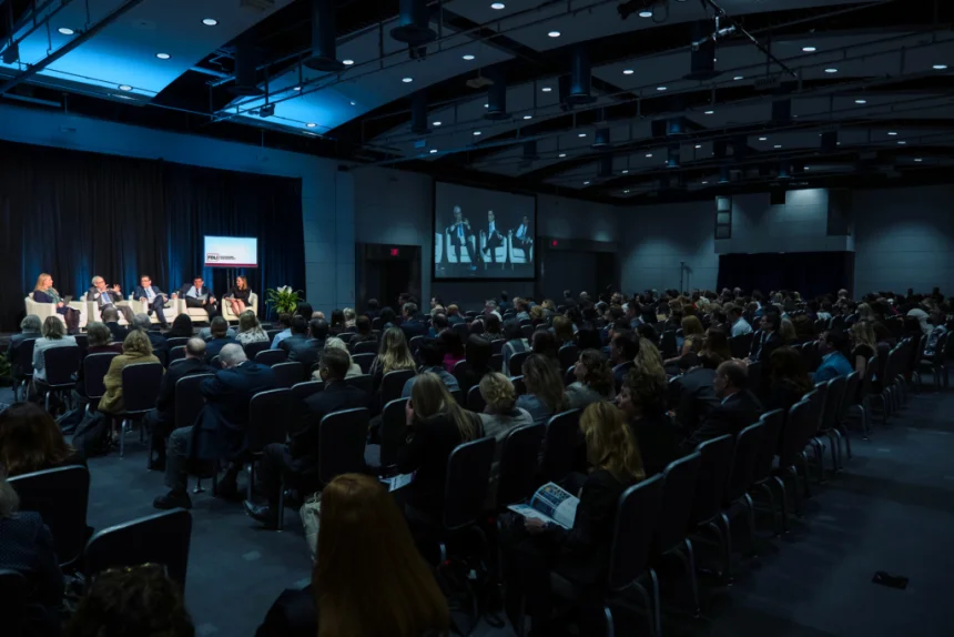 Image of the annual conference - an auditorium of people staring at a lit stage with 5 panelists.